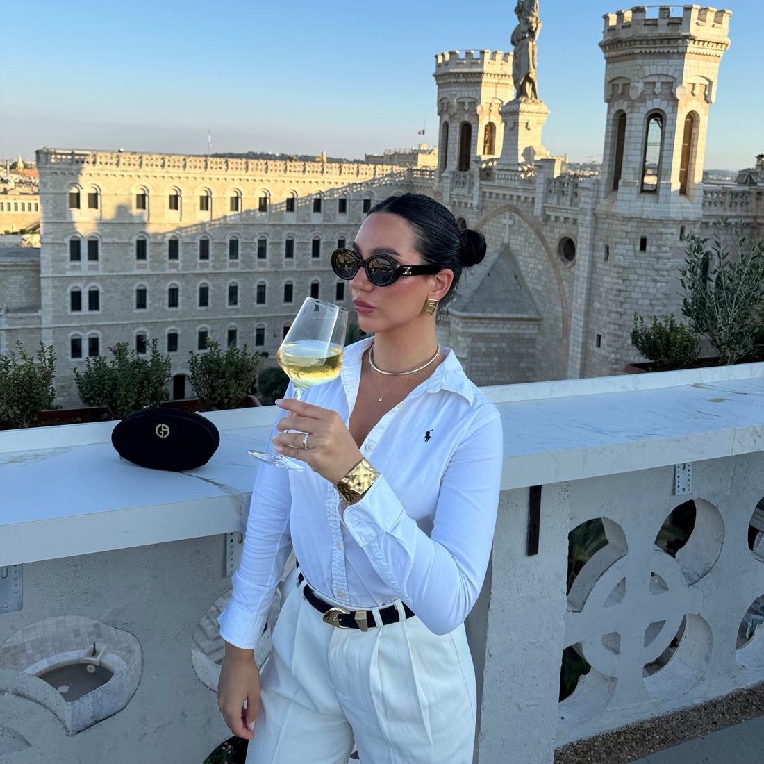 Authentic Polo Ralph Lauren women's white button-down shirt and trousers, holding white wine on a Jerusalem rooftop overlooking Notre Dame de Jérusalem.